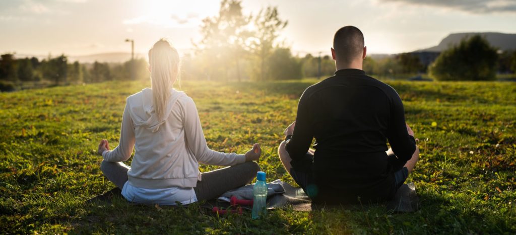 Two people meditating on the ground outside during sunrise mindfulness techniques rheumatology practice NORM